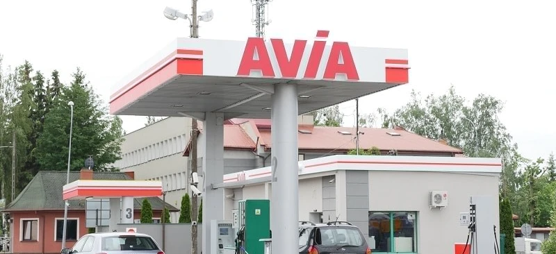 A family car parked at a fuel station with a fuel dispenser in the background. The vehicle's bumper, mirrors, and license plate are visible. AVIA and SD Eibar logos are also present.