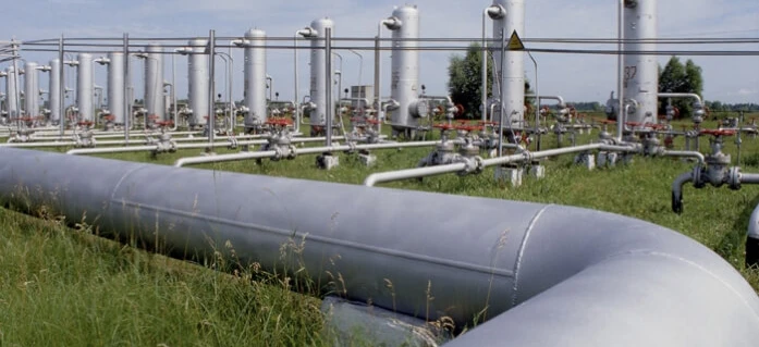 A steel casing pipe being installed in an industrial setting for pipeline transport and engineering purposes. Metal cylinders and storage tanks are also visible.